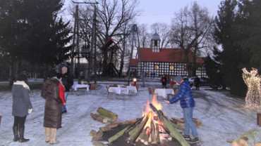 Zdjęcie przedstawia plac przed kościołem z rozpalonym ogniskiem i przygotowanymi stołami. Tu mieszkańcy będą biesiadować po śpiewaniu kolęd w kościele.