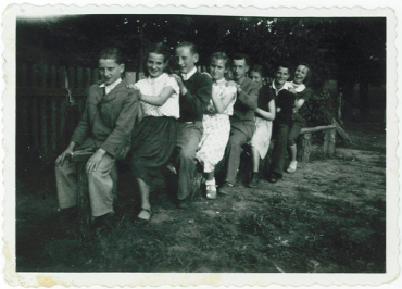 Zdjęcie przedstawia zabawne zdjęcie młodzieży pozującej na ławie w gęsim szyku